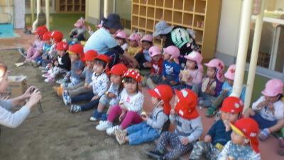ピンク色と赤色の帽子を被った園児たちが横1列に並んで座って、お芋を食べている写真