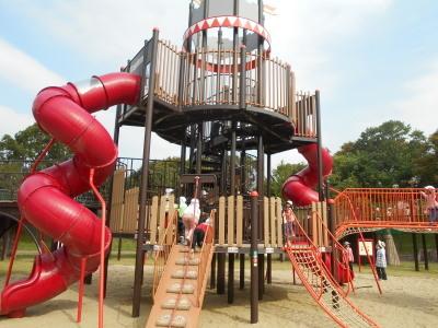 赤い曲がりくねった大きな滑り台のある大型遊具で子ども達が遊んでいる写真