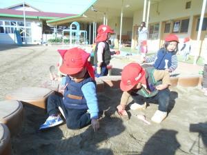 砂場コーナで赤い帽子を被った園児がスコップを持って砂を掘って遊んでいる写真