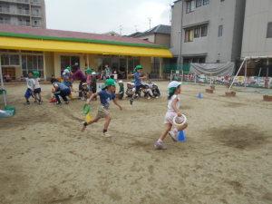 園庭で、輪っかの形のバトンを持ちリレーをする子ども達の写真