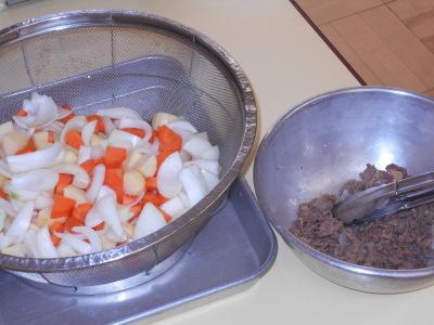 細かく切られたジャガイモ、ニンジン、玉ねぎの入ったざると、茶色の食材がはいったボウルとトングの写真