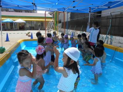 プールの中で先生の周りに集まった子ども達が笑顔で水遊びを楽しんでいる写真