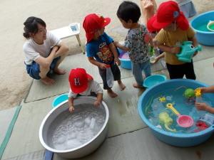 2個のたらいの周りで遊ぶ4名の園児と見守るお母さんの写真