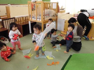 0歳児の園児達が傘袋に紙をいれて遊んでいる写真