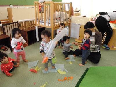 0歳児の園児達が傘袋に紙をいれて遊んでいる写真