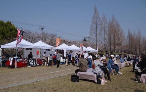 出店店舗のテントが並び食事のできるスペースに腰掛けられる台が置かれ沢山のお客さんで賑わっている様子の写真