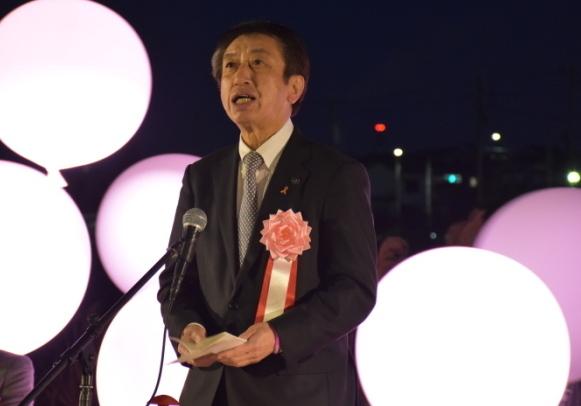 暗闇の中点灯したピンクの風船だけがひかり、その前であいさつをしている市長の写真