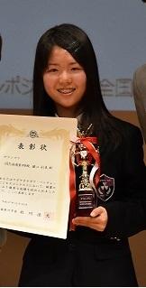 堀江 彩美さんが賞状とトロフィーを持ちながら笑顔で表彰されている写真