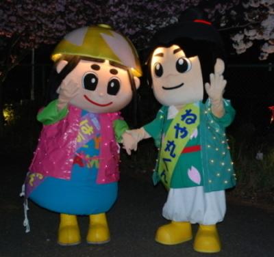 桜の木の下で、光る衣装を身につけたはちかづきちゃんとねや丸くんの写真