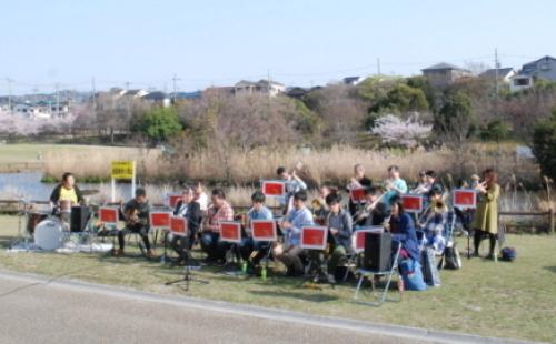 市民コンサートの参加者が芝生の上でいろいろな楽器を演奏している写真