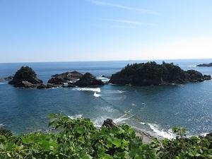 海の浅瀬に小さな島が浮かんでおり、陸と島の間に波がたっている黒島での婦夫波(めおとなみ）の写真