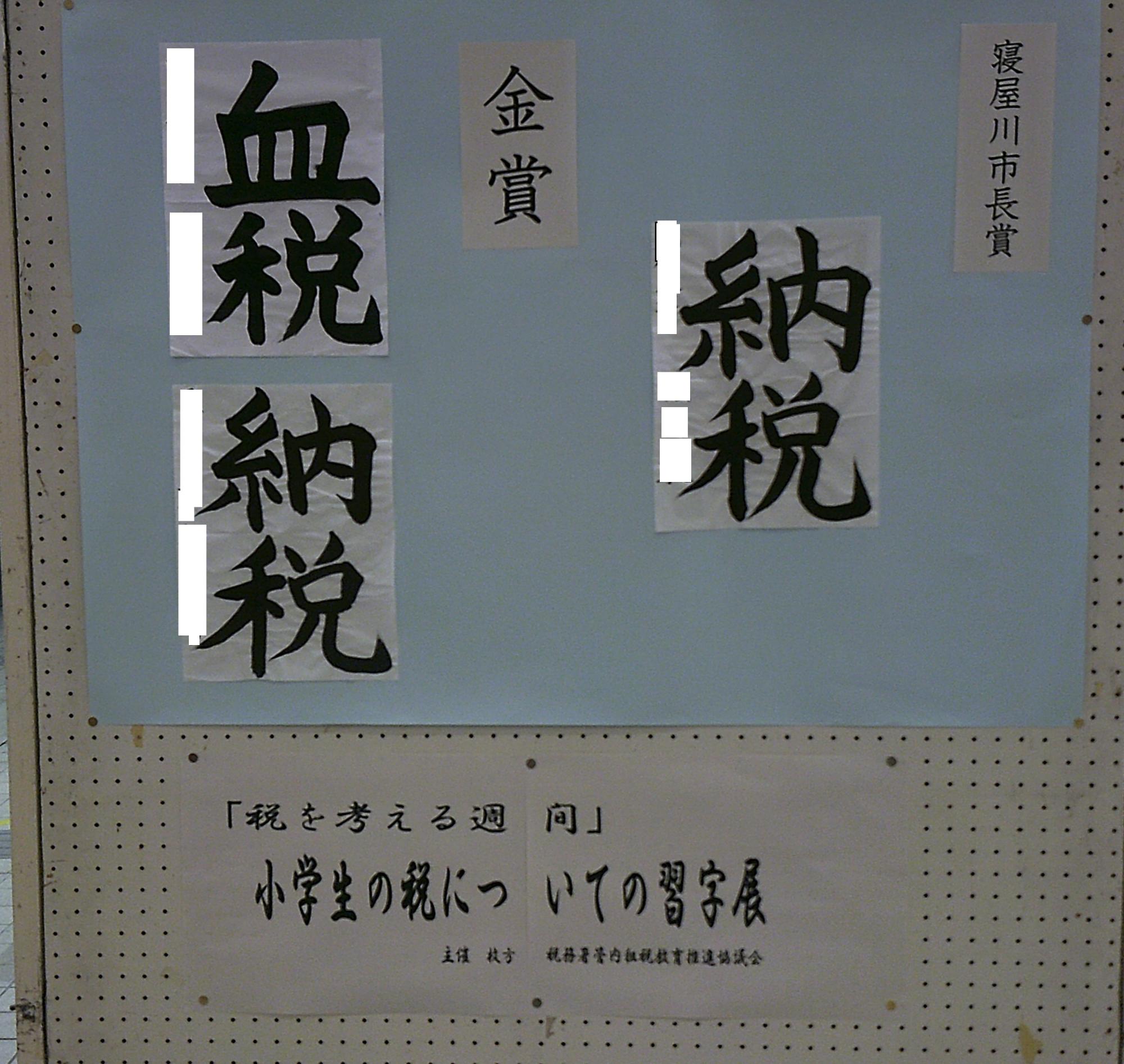 「税を考える習慣」小学生の税についての習字展を書かれた貼り紙の左側に、水色の模造紙が貼られていて寝屋川市長賞と金賞を受賞した「納税」を書かれた習字の作品が展示されている写真