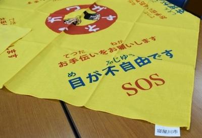 黄色い障害者支援バンダナの「お手伝いをお願いします 目が不自由です SOS」と書かれている部分を写している写真