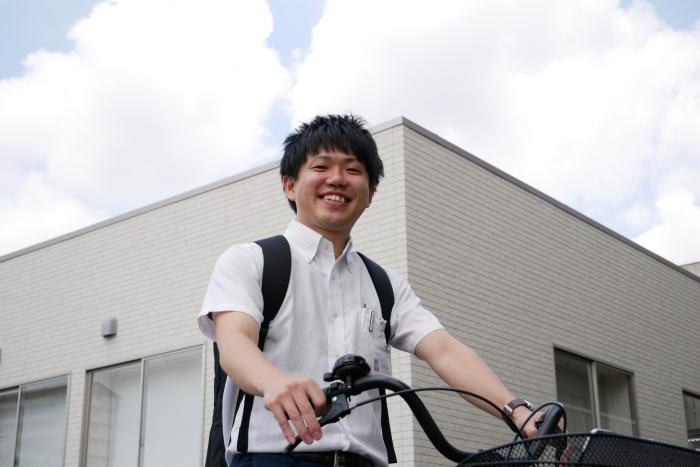 リュック姿で自転車に乗っている笑顔の山本さんの写真