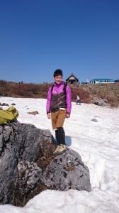 雪が積もっている岩の近くに立っている石田さんの写真