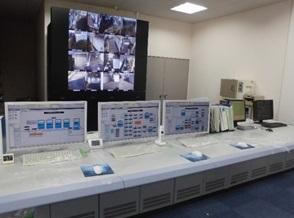 デスクに設置された3台のパソコンとモニターに映し出された監視カメラ映像の写真