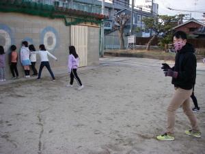 校庭で子ども達が壁にくっついて遊んでおり、学童保育の先生も一緒に遊んでいる写真