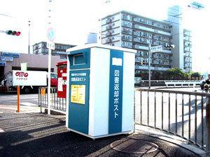 郵便ポストの横に設置されている東寝屋川市駅の白と青色の返却ポストの写真